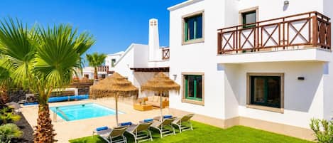 A modern two-story building with a swimming pool, outdoor seating, and a well-maintained lawn.