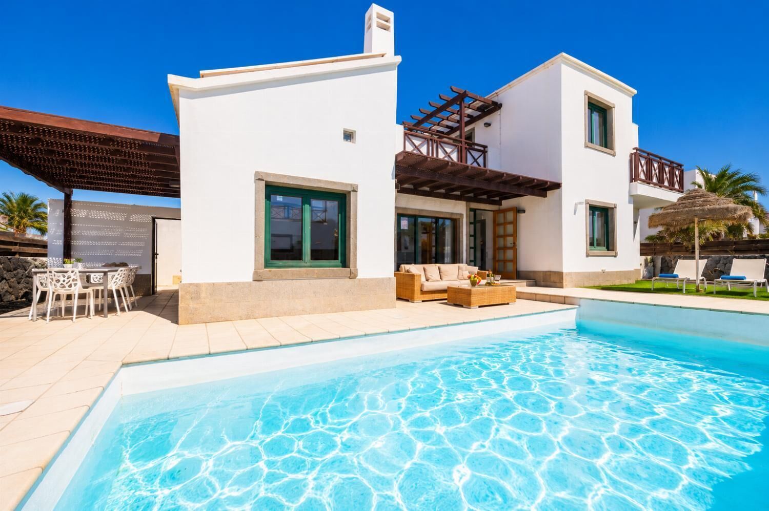 Une maison moderne à deux étages dotée d’une piscine, de mobilier d’extérieur et d’une pergola.