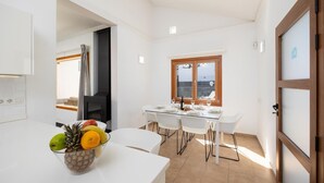A modern kitchen with white cabinets, a dining area with a glass table, and a view through a window. - Villa Dacil - Three Bedroom Villa, Sleeps 6 (Playa Blanca)