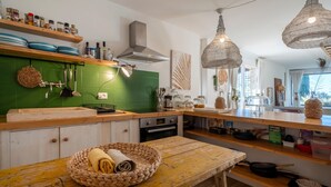 Une cuisine avec des carreaux verts, des étagères en bois, des ustensiles suspendus et des paniers tressés.
