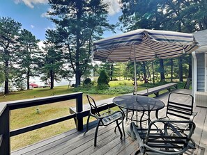 A deck with a table and chairs, an umbrella, and a view of a lake and trees. - Lake Shore by Taylor Made Deep Creek (Swanton)