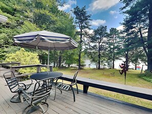 A deck with outdoor furniture, including a table and chairs, and a striped umbrella. - Lake Shore by Taylor Made Deep Creek (Swanton)