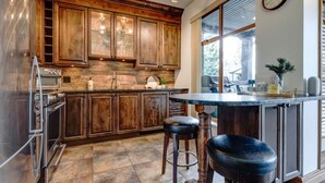 A kitchen with wooden cabinets, a built-in oven, a large window, and a bar area with stools. - Central 2BR with Prime Amenities (Whistler)