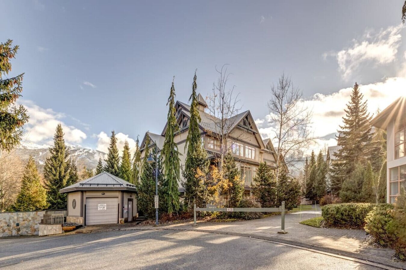 A large, multi-story house with a garage, surrounded by tall trees and a mountain backdrop.