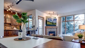 A modern living room with a fireplace, a dining area with a wooden table, and a kitchen with wooden cabinets. - Central 2BR with Prime Amenities (Whistler)