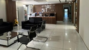 Hotellin aula, jossa on vastaanottotiski, oleskelualue ja jääkaappi.