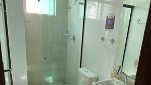 Moderni kylpyhuone, jossa on lasiseinällä varustettu suihku, wc, pesuallas ja peili.