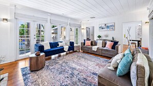Ein geräumiges Wohnzimmer mit großem Fenster, einem blauen Sofa, einem braunen Sofa und einem gemusterten Teppich.