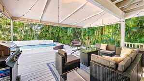 Ein überdachter Außenbereich mit Pool, Gartenmöbeln und üppiger Bepflanzung.