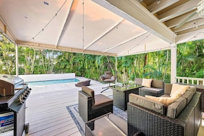 Ein überdachter Außenbereich mit Pool, Gartenmöbeln und üppiger Bepflanzung.