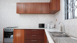 A modern kitchen with wooden cabinets, a microwave, toaster, and a sink. - Luxurious Apartment Complex Kumasi (Kumasi)