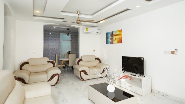 A modern living room with two beige sofas, a glass coffee table, a flat-screen TV, and a ceiling fan. - Luxurious Apartment Complex Kumasi (Kumasi)