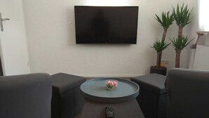 A modern living room with a flat-screen TV mounted on the wall, two armchairs, a small coffee table with a bowl and remote, and two potted plants. - Vacation apartment near Baden-Baden (Bühl)