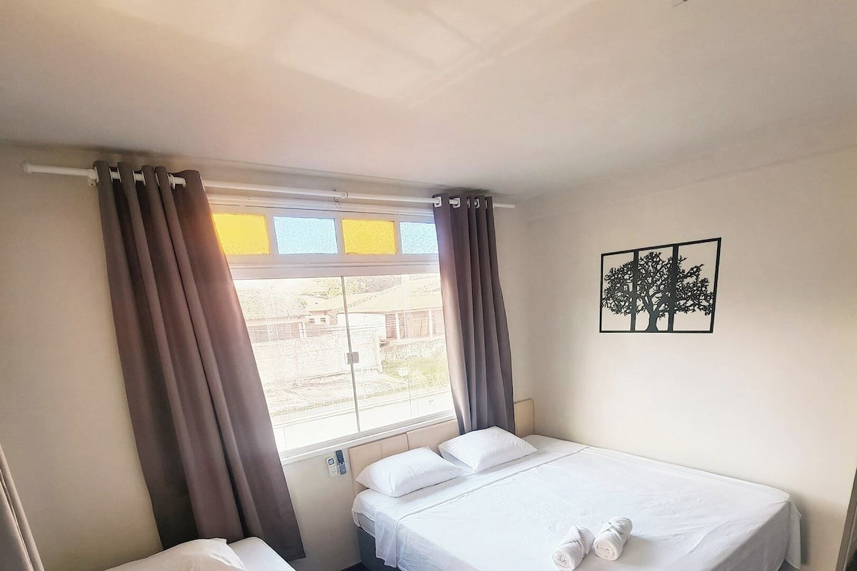 Ett hotellrum med två separata sängar, ett fönster med gardiner, ett konstverk som hänger på väggen och utsikt över omgivningen.