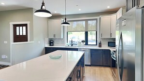 A modern kitchen with a large island, stainless steel appliances, and a view of the outdoors. - Heavenly Summit by Taylor Made Deep Creek (McHenry)