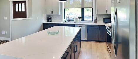 A modern kitchen with a large island, stainless steel appliances, and a view of the outdoors.