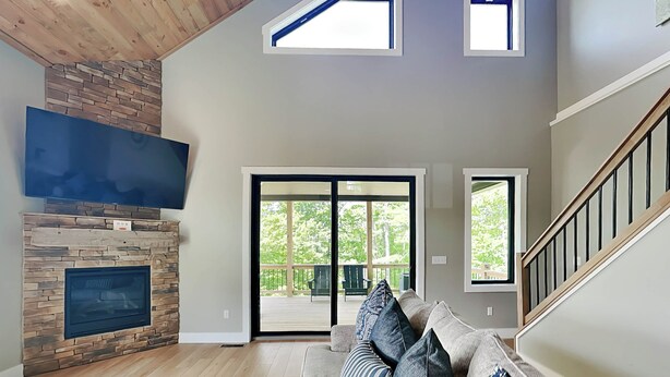 A spacious living room with a stone fireplace, a large flat-screen TV, a wooden coffee table, and a sofa with multiple cushions. - Heavenly Summit by Taylor Made Deep Creek (McHenry)