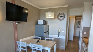 A compact kitchen with a dining area, a microwave, a refrigerator, a telephone, and a television mounted on the wall. - Superbe Vue Mer 2 Pièces Climatisé Les Restanques (Grimaud)