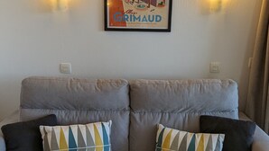 A bed with a striped blanket and two pillows with geometric patterns. Above the bed, there is a framed picture of a town scene with the text "GRIMAUD". - Superbe Vue Mer 2 Pièces Climatisé Les Restanques (Grimaud)