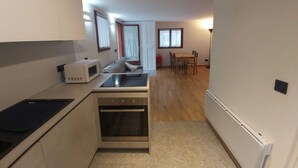 A compact kitchen with a microwave, stove, and oven, leading to a dining area with a table and chairs.