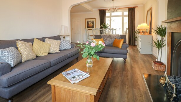 Una sala de estar con un sofá gris, una mesa de centro de madera con revistas, y un florero con flores.