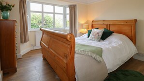 Un dormitorio con una cama de madera, una mesita de noche con lámpara, una ventana con cortinas y un radiador.