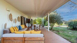 Un espace extérieur abrité, aménagé avec un banc en bois, un canapé avec des coussins et une table avec des chaises.