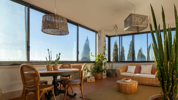 Une pièce spacieuse comprenant une table à manger, des chaises, un canapé et de grandes fenêtres donnant sur la verdure.