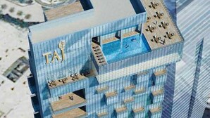Un hôtel de grande hauteur, reconnaissable à son grand panneau « TAJ », doté de nombreux balcons et d’une piscine sur le toit.