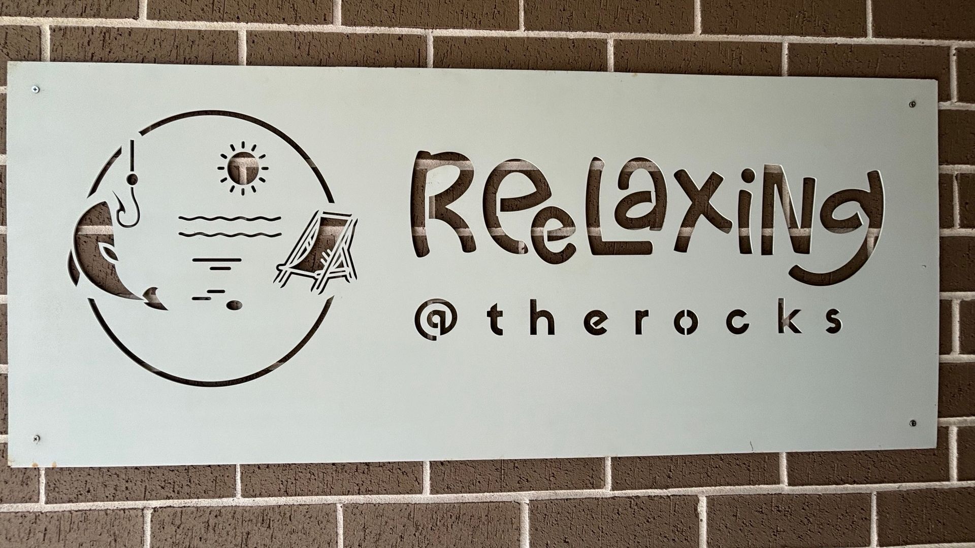 Une enseigne avec le mot « REAXING » et un logo représentant un soleil, des vagues et un parasol de plage.