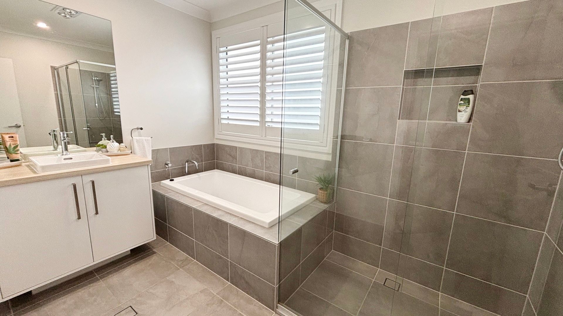 Ein modernes Badezimmer mit einer Badewanne, einer Dusche, einem Waschbecken und einem Fenster mit Jalousien.