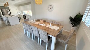 Una cuina moderna amb armaris blancs, un frigorífic d'acer inoxidable i una zona de dinar amb taula de fusta i cadires de vimbles.
