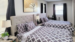 A modern bedroom with two beds, a tufted headboard, a side table with a lamp, and a framed picture.