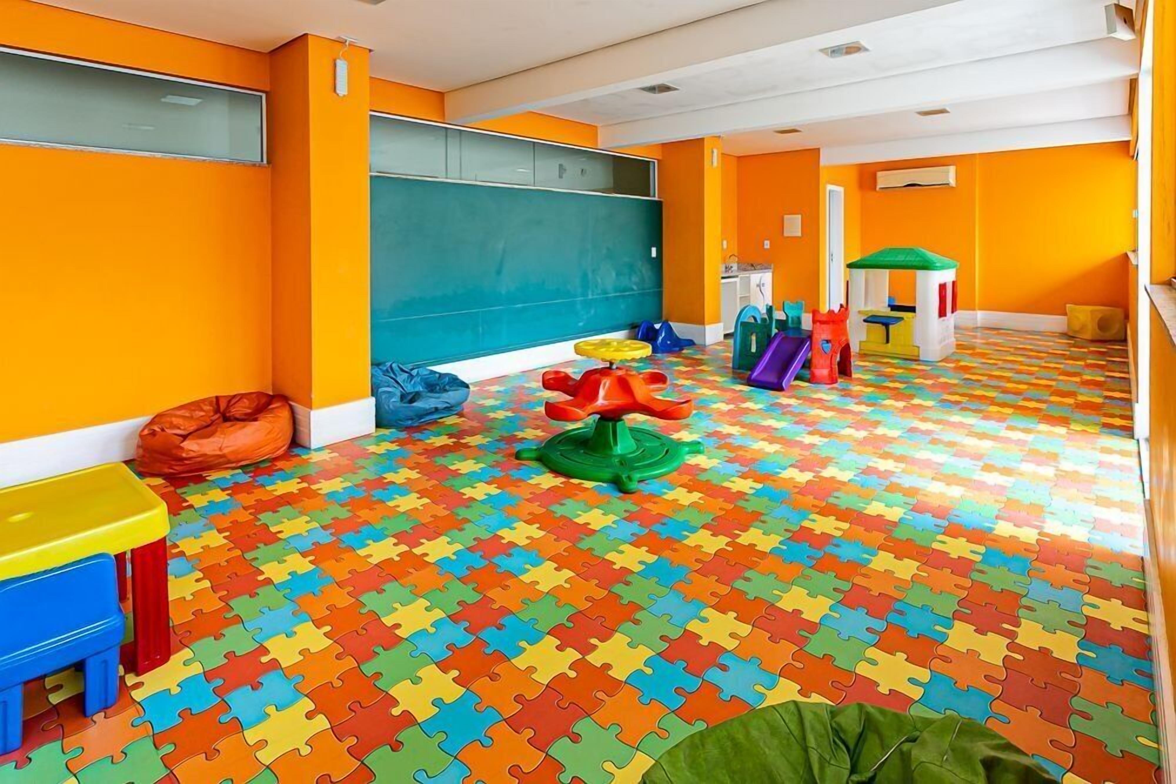 Une salle de jeux aux couleurs vives, avec un sol décoré de motifs de puzzle, un tableau noir et divers éléments de jeu.