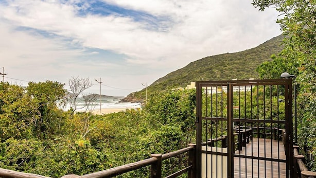 Eine Holzterrasse mit einem Metallgitter, umgeben von dichtem Grün und mit Blick auf einen Strand.