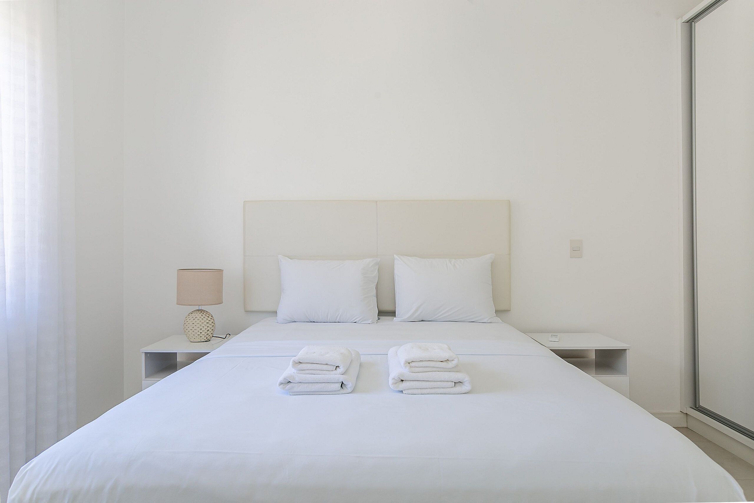 Ein Hotelzimmer mit einem großen Bett, zwei weißen Kissen, einem Nachttisch mit einer Lampe und zwei Handtüchern auf dem Bett.