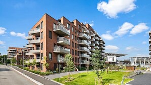 A modern apartment building with multiple balconies, a well-maintained lawn, and a clear blue sky. - Helt ny Leilighet i Oslo Helsfyr (Oslo)
