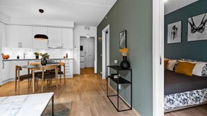 A modern kitchen with white cabinets, a dining table with chairs, and a black pendant light. - Helt ny Leilighet i Oslo Helsfyr (Oslo)
