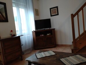 Une pièce avec un meuble en bois, une télévision, un escalier et une fenêtre avec des rideaux.