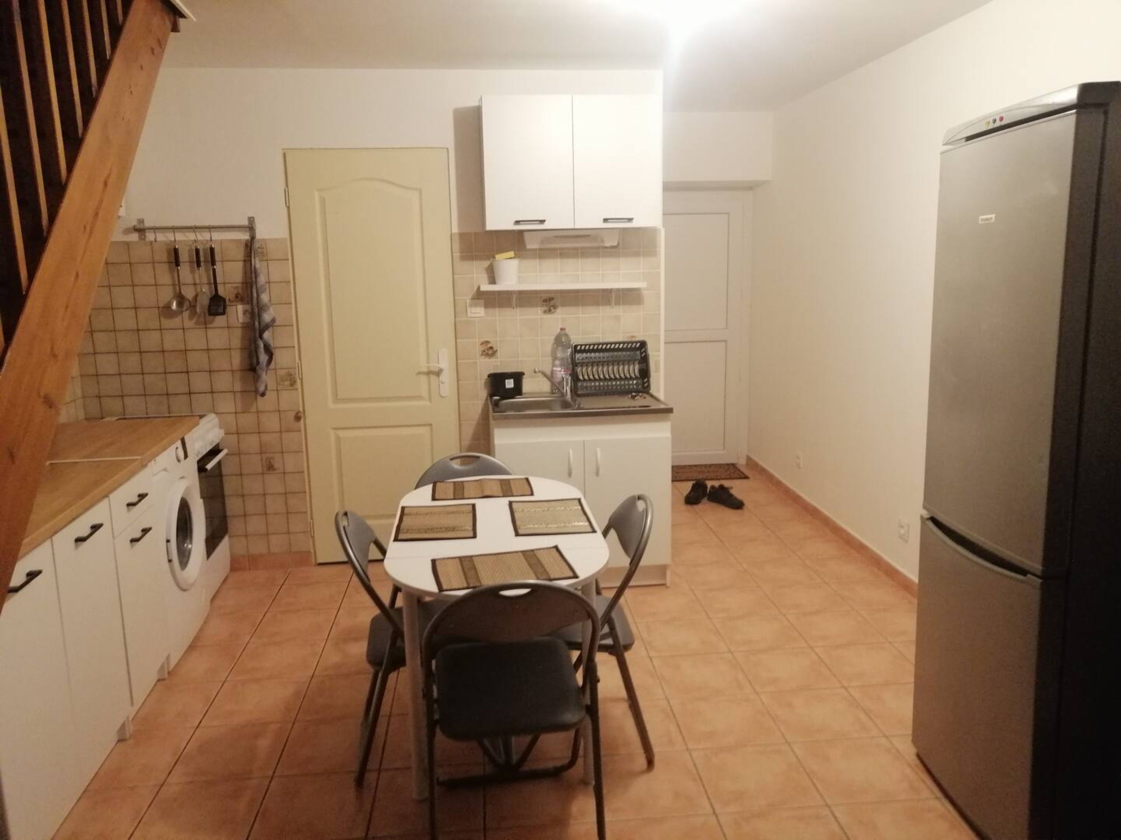 A compact kitchen with a dining table, chairs, a washing machine, and a refrigerator.