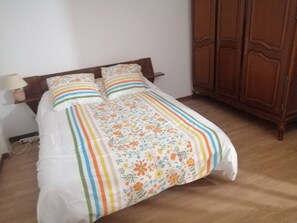 Un lit avec une couvre-lit à motifs floraux et des oreillers à rayures, une tête de lit en bois, une table de chevet avec une lampe et une armoire en bois.