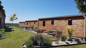 A row of wooden cabins with outdoor seating and garden beds. - Ferme du Château (Monampteuil)