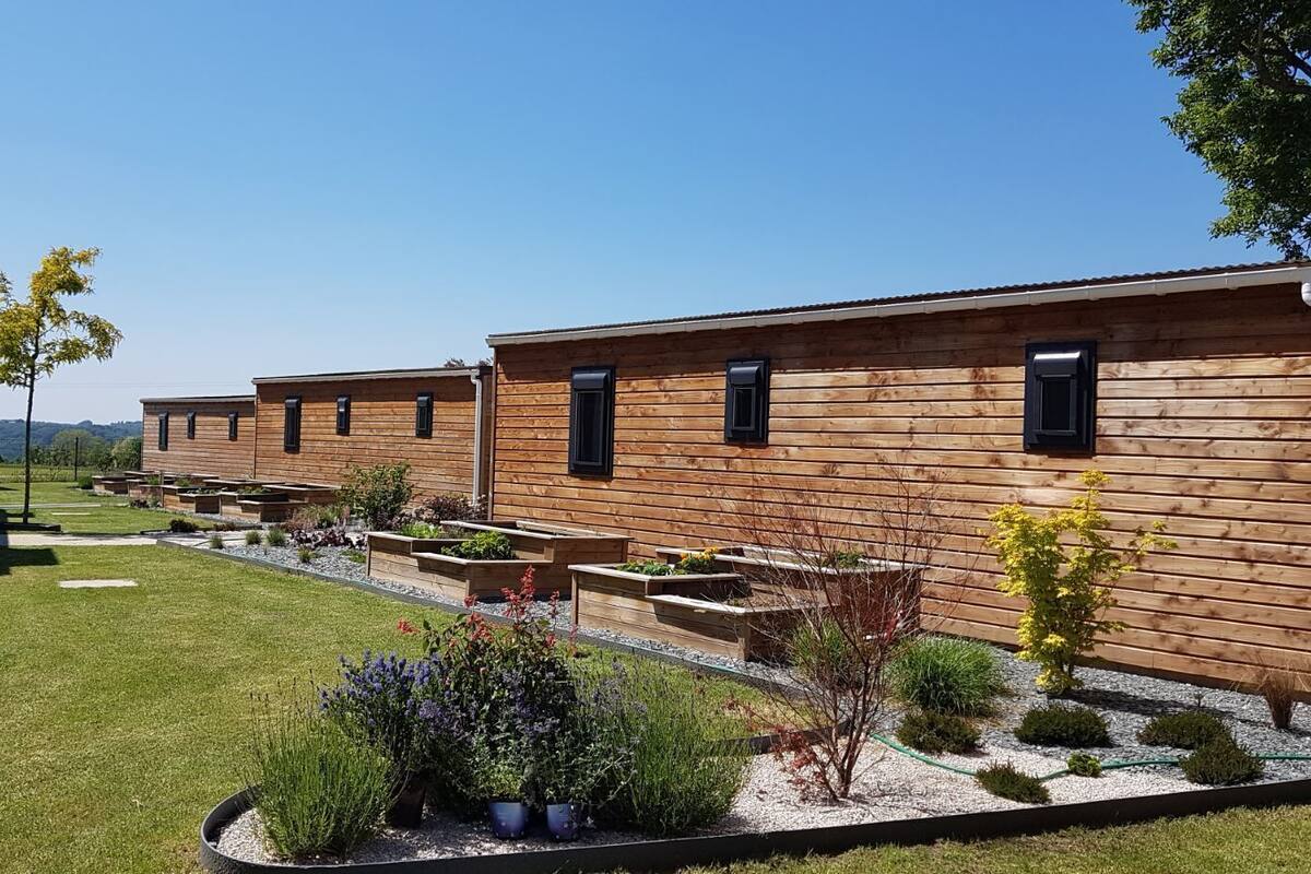 Une rangée de cabanes en bois, dotées d’espaces extérieurs pour s’asseoir et de parterres de jardin.
