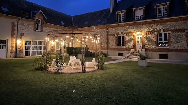 A courtyard with a gazebo, outdoor seating, and a stone building with multiple windows and a staircase. - Ferme du Château (Monampteuil)