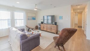 Ein modernes Wohnzimmer mit Sofa, Sesseln, Fernseher und einer Holzkassette.