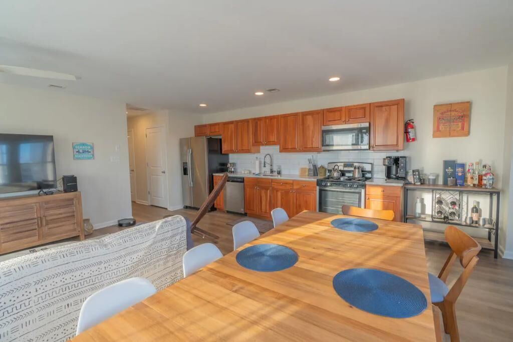 A modern kitchen with wooden cabinets, a central island, and a dining area with a wooden table and chairs.