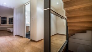 A modern interior with a wooden staircase, a glass door leading to another room, and a wooden floor.