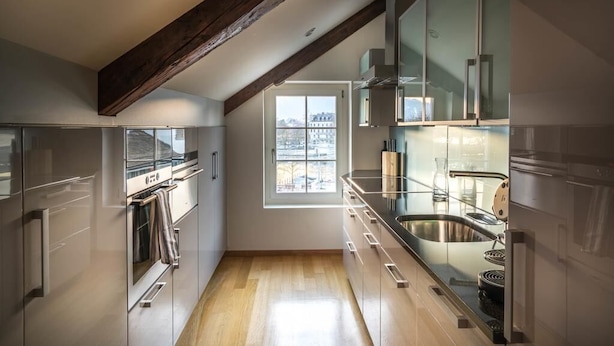 A modern kitchen with wooden beams, a large window, and stainless steel appliances.