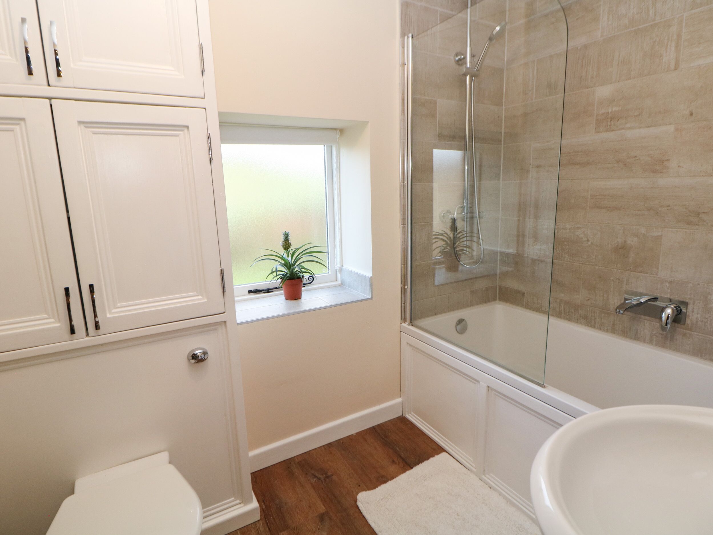Ein Badezimmer mit Dusche, Toilette und einem Fenster mit Pflanze.