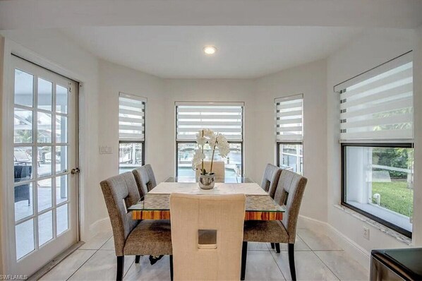 A dining room with a glass-top table, four upholstered chairs, and a vase with flowers.